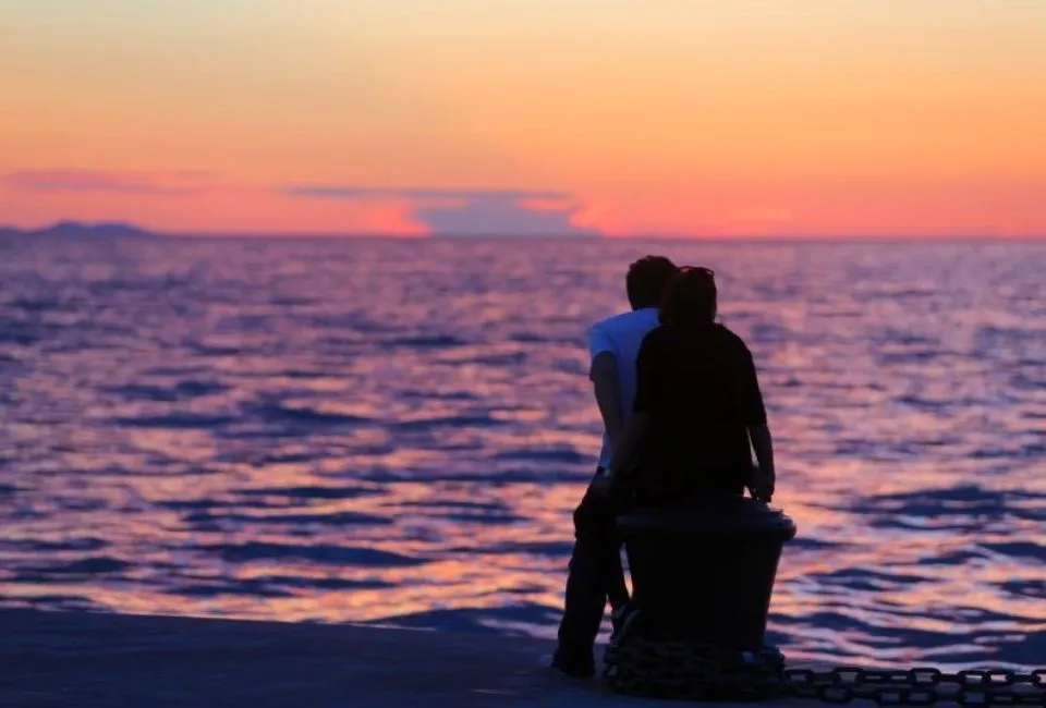 Hình ảnh một người đàn ông và một người phụ nữ đang ngồi cạnh nhau, cô gái đang ôm chàng trai, thể hiện sự gần gũi, ấm áp và lời chúc ngày mới đầy tình cảm.