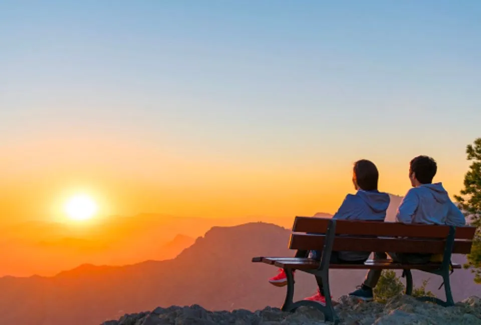 Một cặp đôi lãng mạn đang nắm tay nhau đi dạo trên bãi biển vào lúc bình minh, tượng trưng cho sự khởi đầu tốt đẹp của một ngày mới và tình yêu vững chắc.