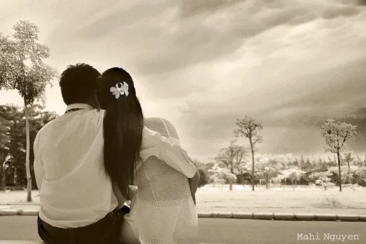 Cặp đôi nắm tay nhau và tựa vai trên bãi biển lúc hoàng hôn